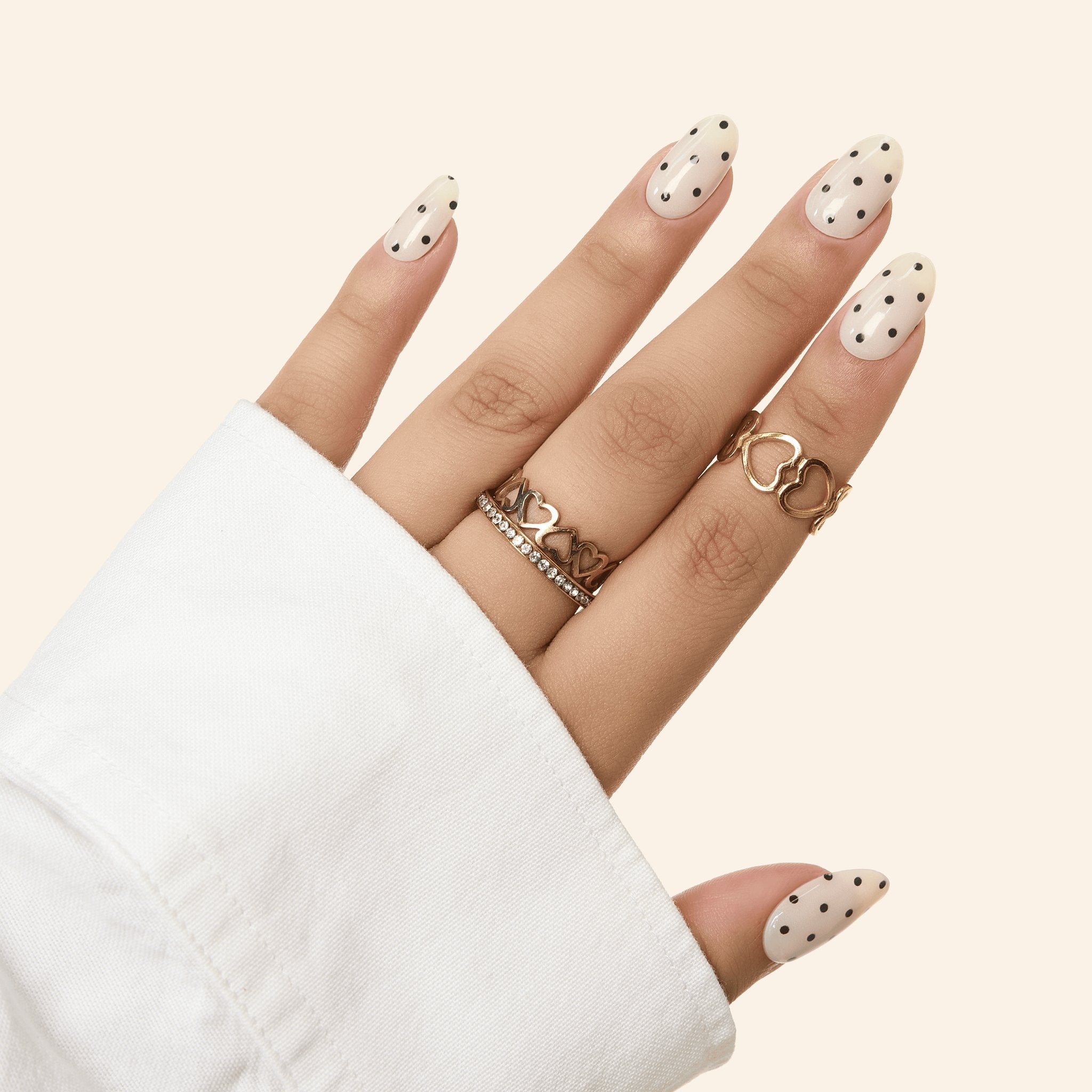 Milky White & Black Polka Dot GEWEL™ semi-cured gel nail stickers on almond nails, hand with gold heart rings
