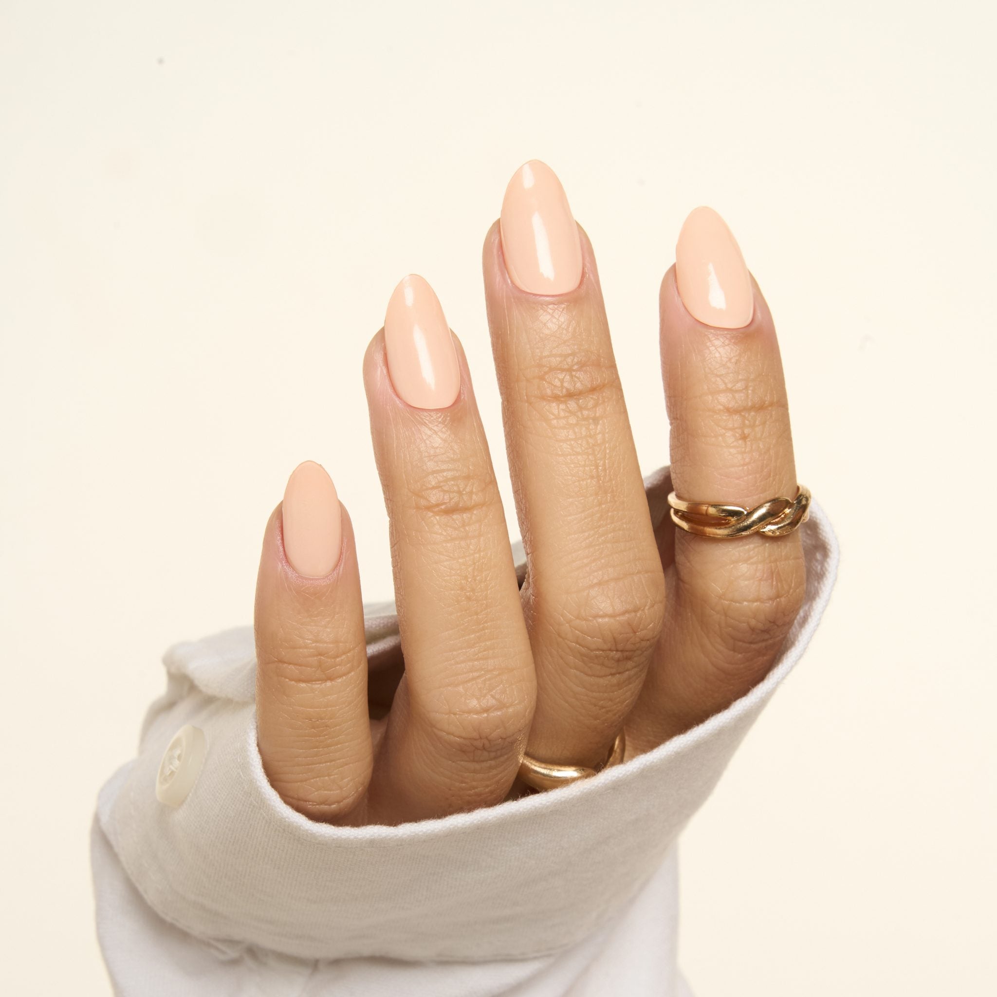 Nude Pink GEWEL™ glossy nude manicure on long almond nails, hand in a cream sleeve
