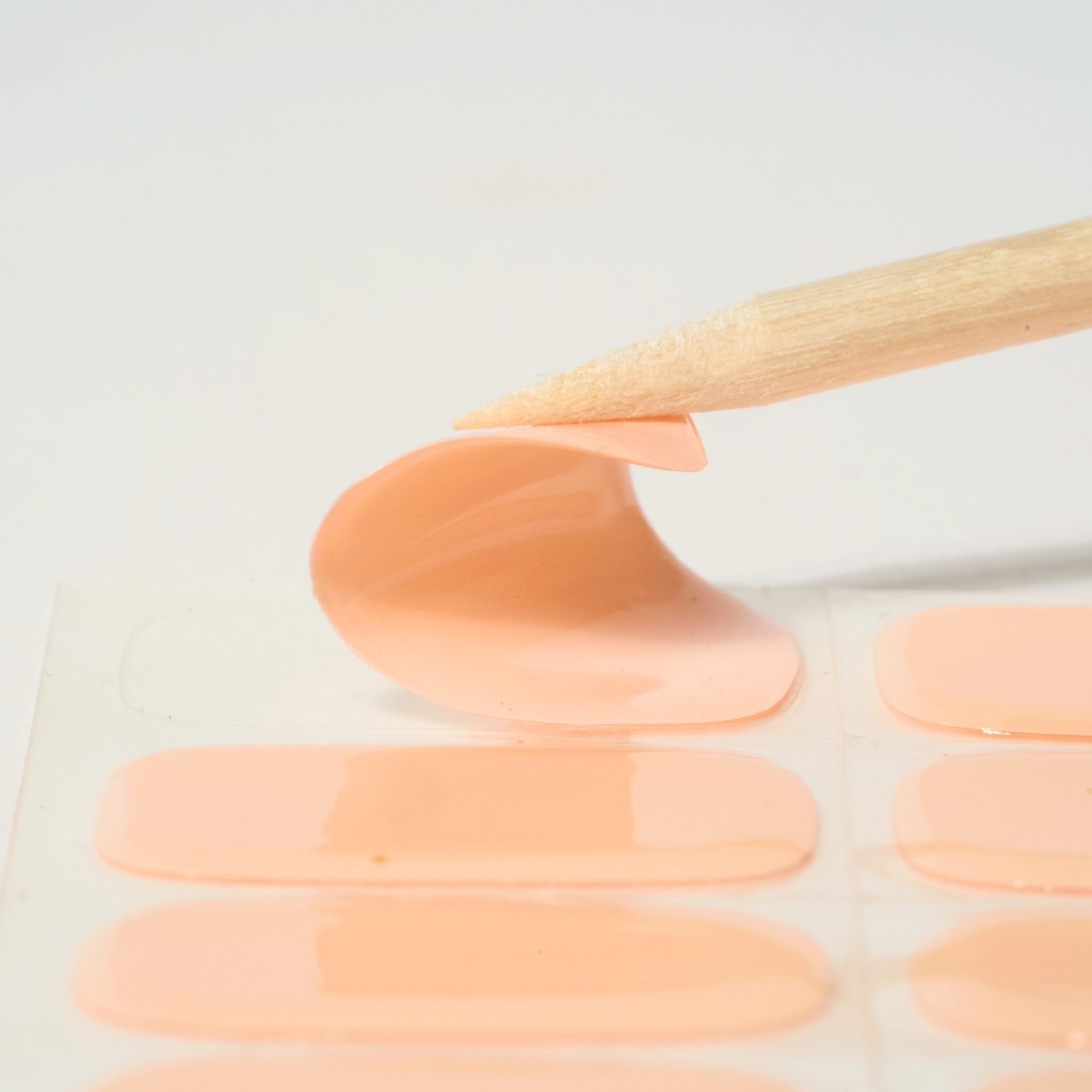 Close-up of a Nude Pink GEWEL™ semi-cured gel nail sticker peeled with a wooden stick